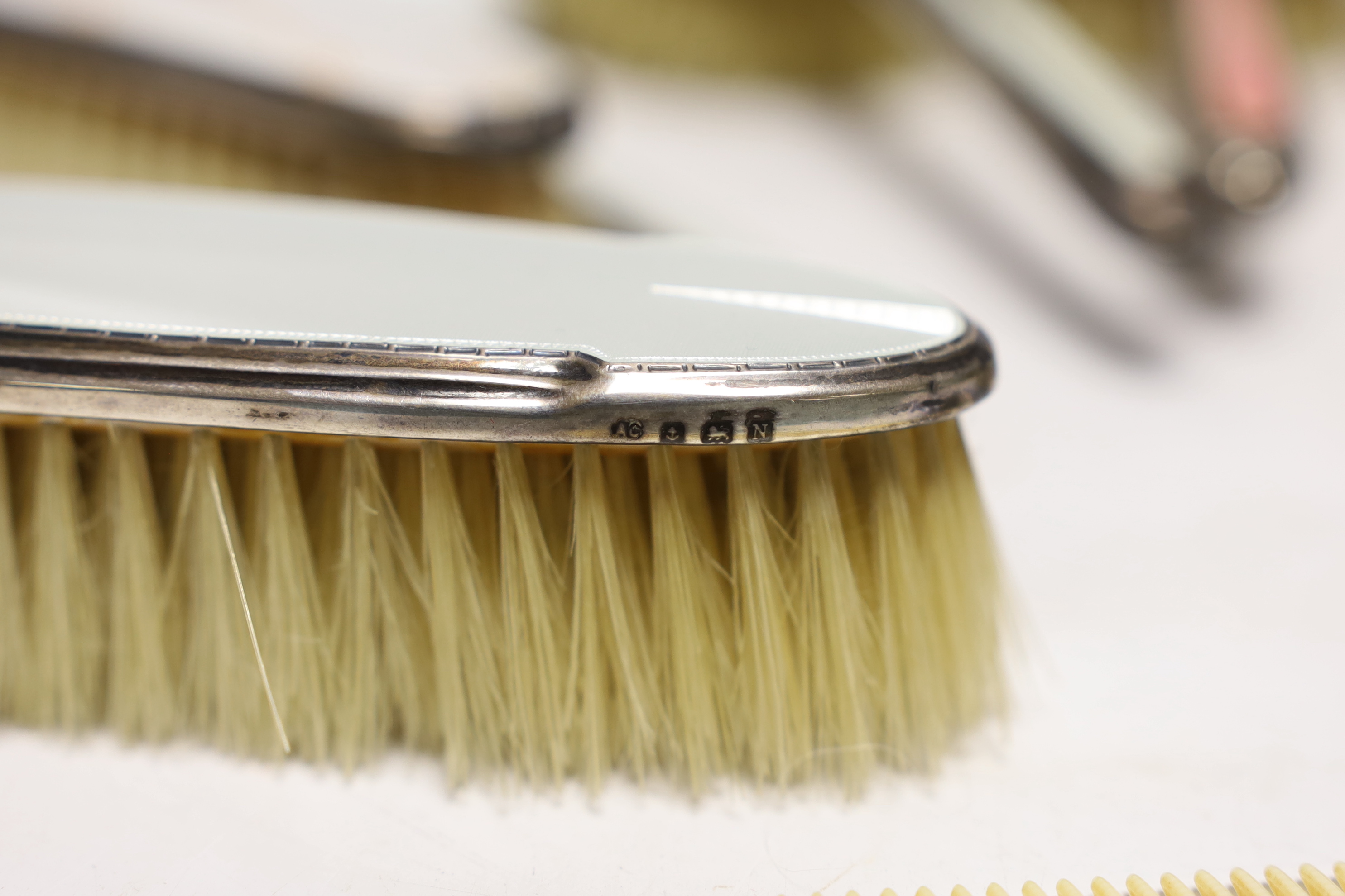 A George VI Art Deco silver, guilloche enamel, blue zircon and marcasite set five piece mirror and brush set and similar enamelled comb, Albert Carter, Birmingham, 1936/7, together with three other later silver and ename